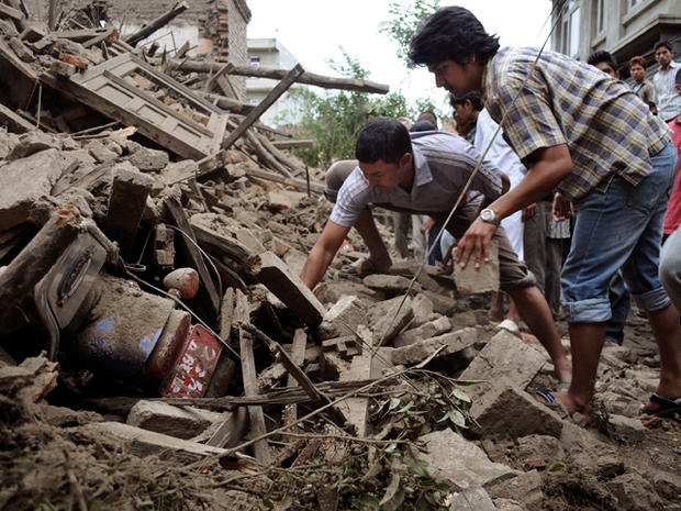Nepalese people try to take out a motorbike buried under the debris  