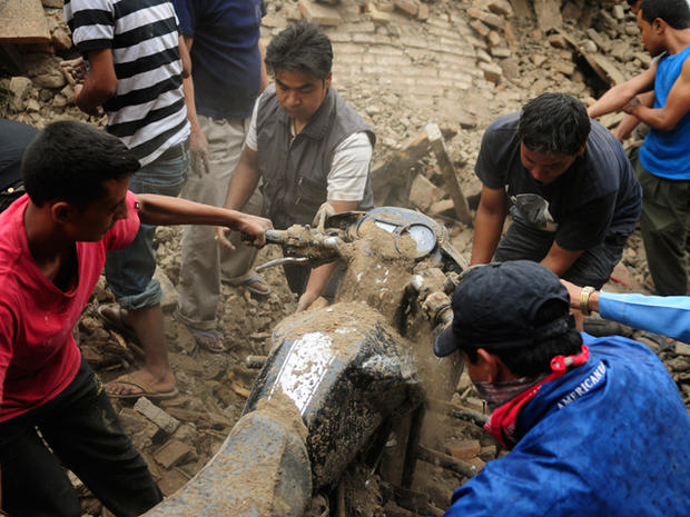 Nepalese people take out a motorbike buried under the debris  