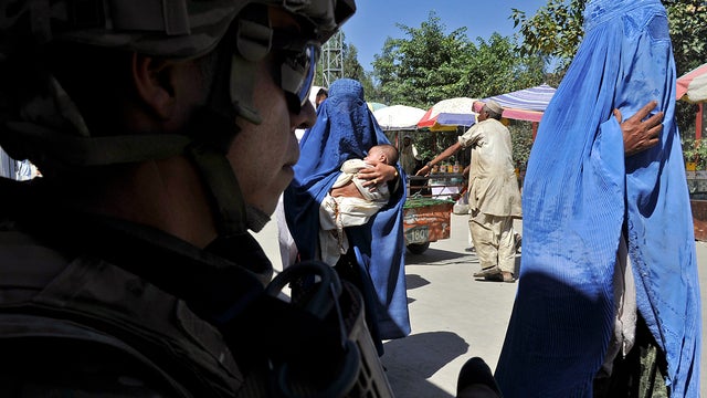 U.S. Army soldier Jose Calzada stands guard in a street during a mission as an Afghan woman walks by in Turkham Nangarhar, Afghanistan, near the border with Pakistan Oct. 2, 2011. Turkham is a border-crossing town in the Nangarhar province of Afghanistan  