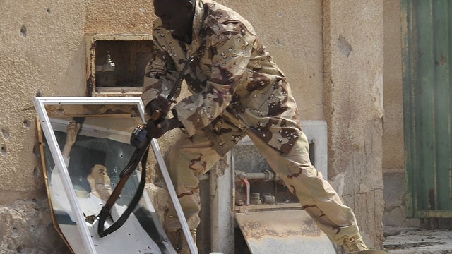 Libyan revolutionary fighter smashes a portrait of Muammar Qaddafi  