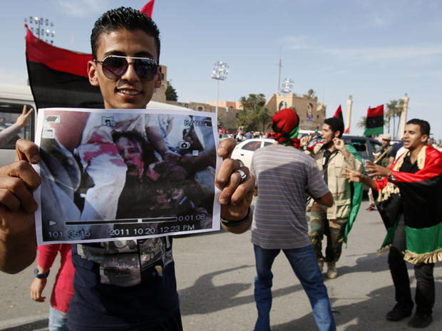 A man holds a photo said to be the body of Moammar Qaddafi 