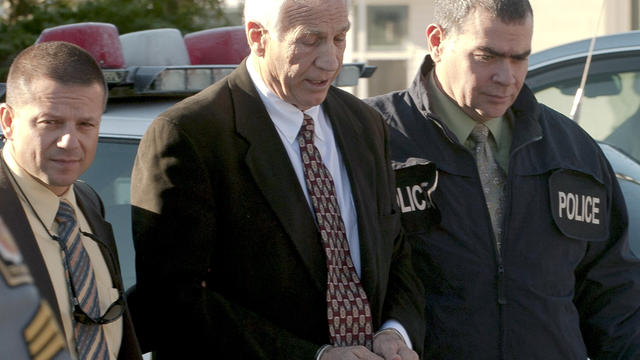 Gerald "Jerry" Sandusky is escorted in handcuffs to a waiting police car 