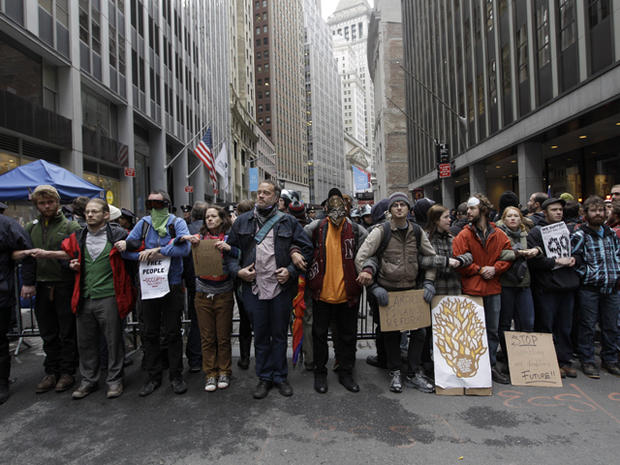 The New York Stock Exchange is seen in the background as demonstrators affiliated with the Occupy Wall Street movement lock arms while blocking Broad Street Nov. 17, 2011, in New York. 