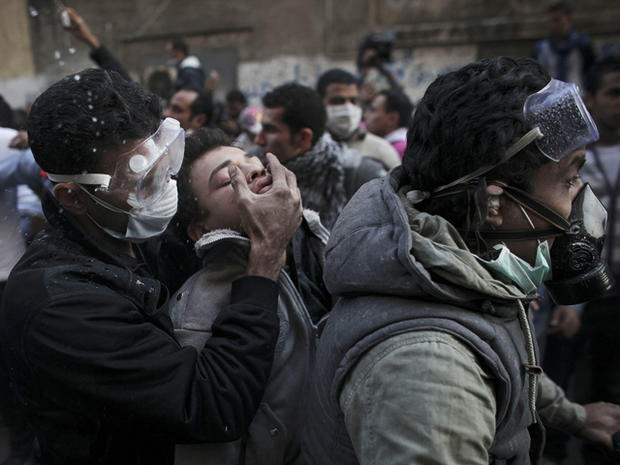 protester overwhelmed by tear gas is aided by two men  