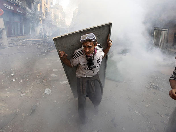 An Egyptian protester using scrap metal as a shield takes cover from tear gas during clashes with security forces near Tahrir Square in Cairo, Egypt, Nov. 23, 2011. 