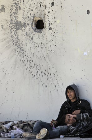Weary rebel fighters rest in the shade of the outside wall of a mosque 