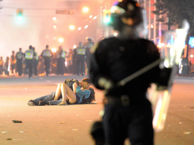 Riot police walk in the street as a couple kiss 