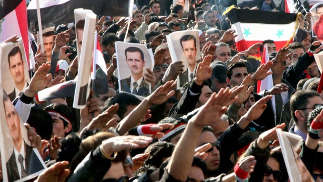 Syrian demonstrators raise posters showing Syria's President Bashar Assad 