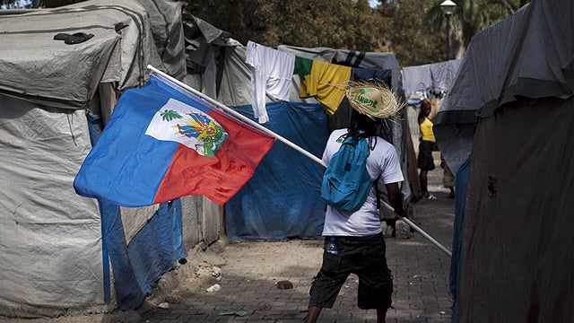 A demonstrator waves a Haitian flag while walking between makeshift tents at the temporary camp in Champ de Mars, across the street from the collapsed National Palace, during a protest to demand new housing in Port-au-Prince, Haiti, Jan. 11, 2012.  