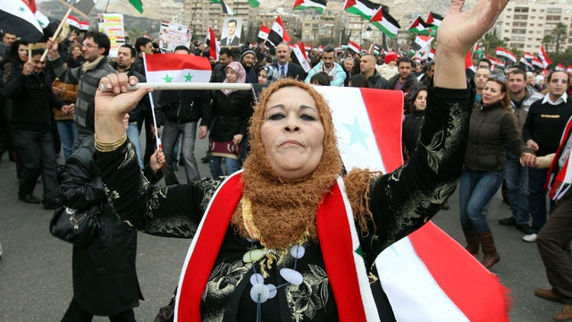 A supporter of Syrian President Bashar Assad holds a national flag while others wave Palestinian flags in the background during a rare public appearance Assad made in Damascus, Syria, Jan. 11, 2012. 