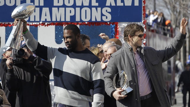 Justin Tuck holds the Vince Lombardi Trophy, and Eli Manning, holding the Halas Trophy 