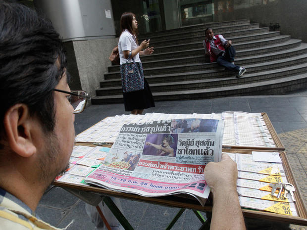 A Thai lottery vendor reads a newspaper showing a photo of the late singer Whitney Houston  