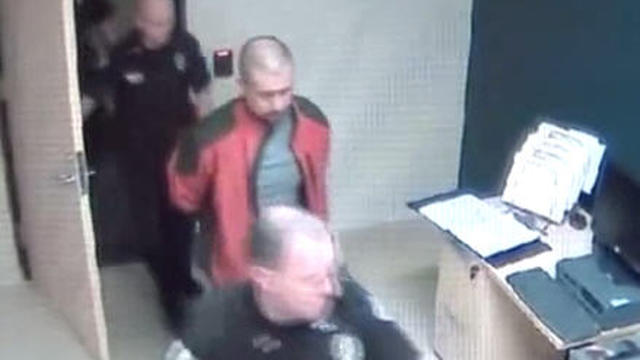 Still from video from inside Sanford, Fla. police station shows a handcuffed George Zimmerman being led by police 