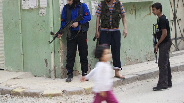 In this Monday, May 14, 2012 photo, a girl walks past Syrian rebels at Khaldiyeh neighborhood in Homs province, central Syria.  