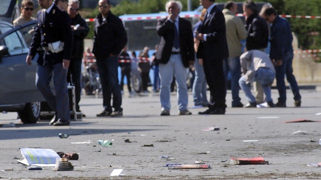 Italian policemen, background left, walk on site where explosive device went off outside "Francesca Morvillo Falcone" high school in Brindisi, Italy, Saturday 