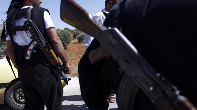 An armed Free Syrian Army solider, left, with the colors of the Syrian revolutionary flag painted on his weapon, stands guard at a checkpoint on the outskirts of Idlib, Syria, June 3, 2011. 