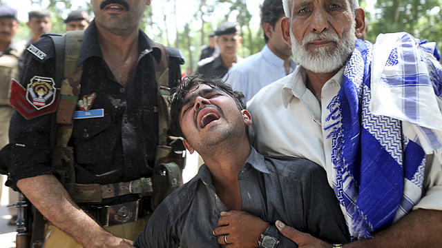 A Pakistani man, center, reacts after learning of the death of his brother at the site of a bus explosion on the outskirts of Peshawar, Pakistan, June 8, 2012.  