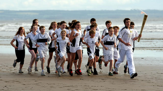 Joseph Forrest and children from Madras College run along West Sands beach with the Olympic Torch on June 13, 2012 in St Andrews, Scotland.  