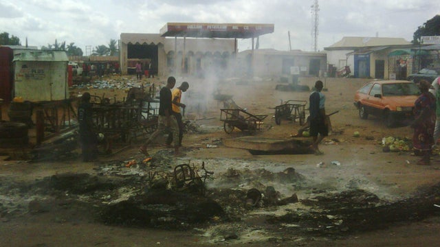 People walk near ashes after the burning of the Dullahi gas station burnt by angry Christian youths in reaction to a bomb attack at the Shalom Church in Kaduna on June 17, 2012. 