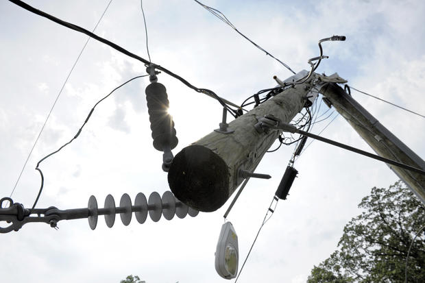 A utility pole is cracked in half by a downed tree on a residential street  