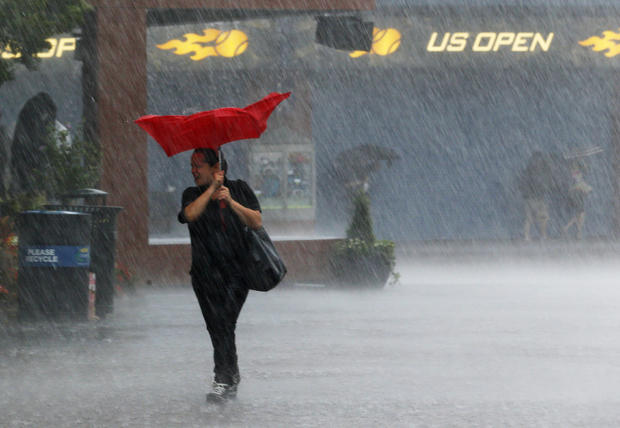 A woman struggles with her umbrella as tennis fans take shelter 