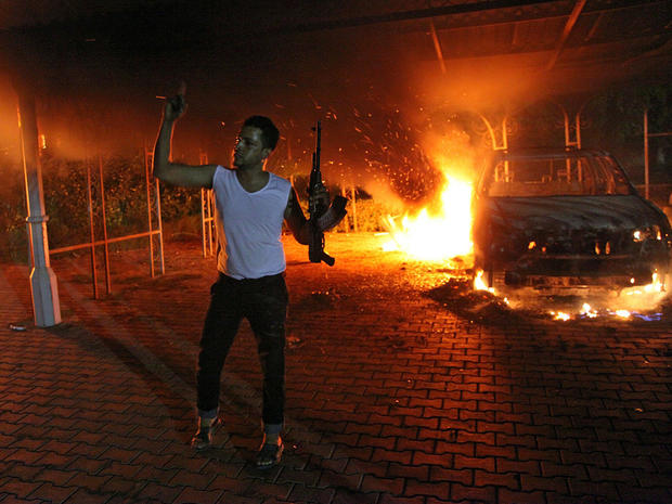 A man waves his rifle as buildings and cars burn after being set on fire inside the U.S. consulate compound in Benghazi 