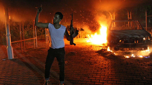 An armed man waves his rifle as buildings and cars are engulfed in flames after being set on fire inside the U.S. Consulate compound in Benghazi, Libya, Sept. 11, 2012. 