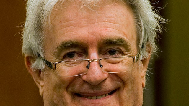 Suspected war criminal and former Bosnian Serb leader Radovan Karadzic smiles as he takes his seat at defense table Tuesday in The Hague 