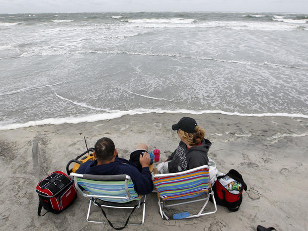 People sit at the edge of beach on North Wildwood, NJ as Sandy churns in the Atlantic 