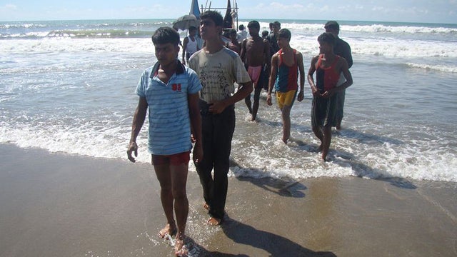 Rohingya refugees, who survived after their overloaded boat heading to Malaysia sank, walk onto the beach 