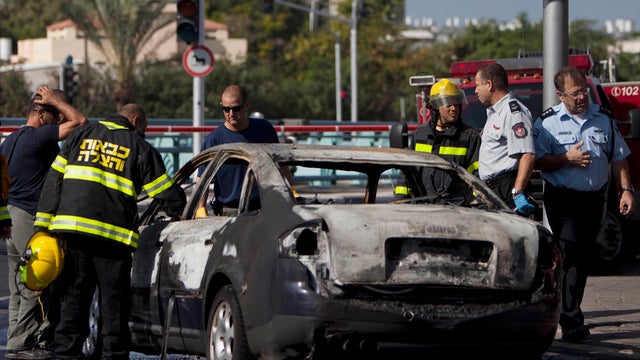 Israeli Police officers and fire brigade inspect a car damaged by shrapnel from a Fajr missile fired by Palestinian militants from the Gaza Strip that was intercepted by the Iron Dome defense system over the central Israeli city of Holon, Sunday, Nov. 18, 
