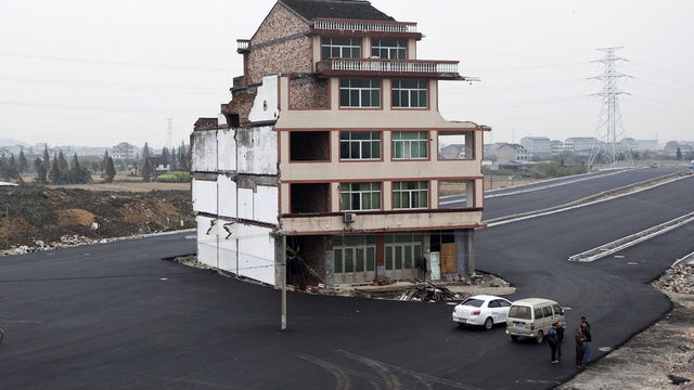  In this Nov. 22, 2012 file photo, people stand near a house sitting in the middle of a new main road on the outskirts of Wenling city in east China's Zhejiang province. Duck farmer Luo Baogen and his wife are the lone holdouts from a neighborhood of once 
