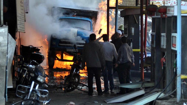 Syrians stand near a burning truck that was destroyed by two car bombs in the Jaramana suburb of Damascus, Syria, Nov. 28, 2012, in this photo released by the Syrian official news agency SANA. 