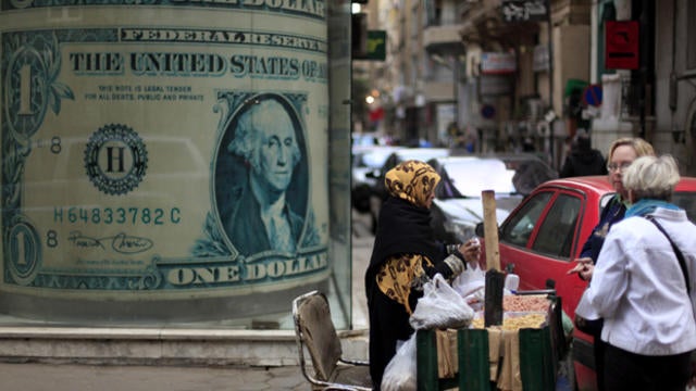 n Egyptian vendor sells nuts in front of a giant poster of a U.S. dollar outside a currency exchange office in Cairo, Egypt, Tuesday, Dec. 25, 2012. 