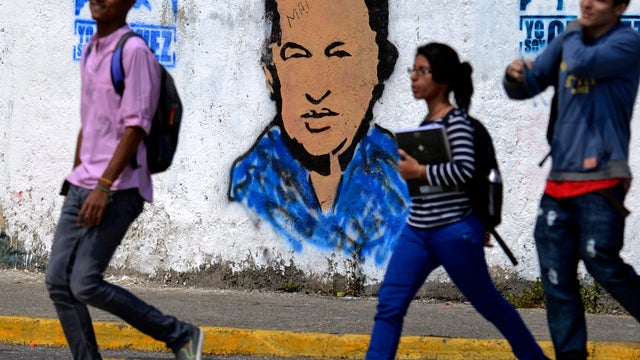 Youngsters walk in front of a banner of Venezuelan President Hugo Chavez in Caracas 