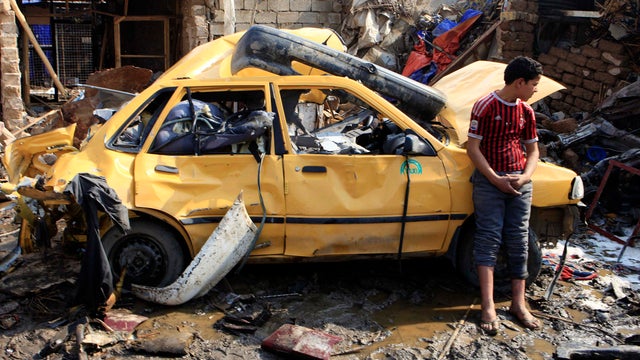 An Iraqi boy stands near a destroyed car at the scene of a car bomb attack in Baghdad 