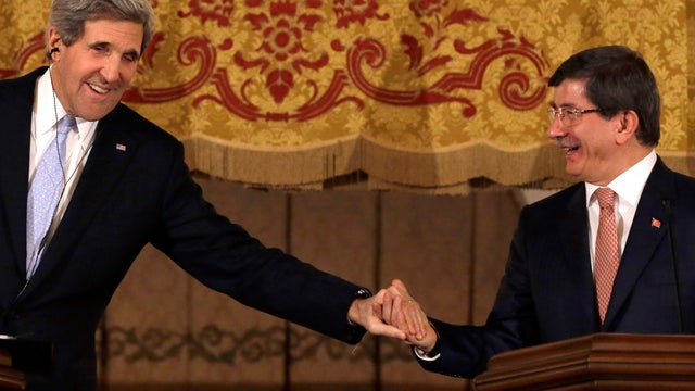 U.S. Secretary of State John Kerry leans over to clasp Turkish Foreign Minister Ahmet Davutoglu's hand at the end of a news conference at Ankara Palace in Ankara, Turkey, March 1, 2013. 