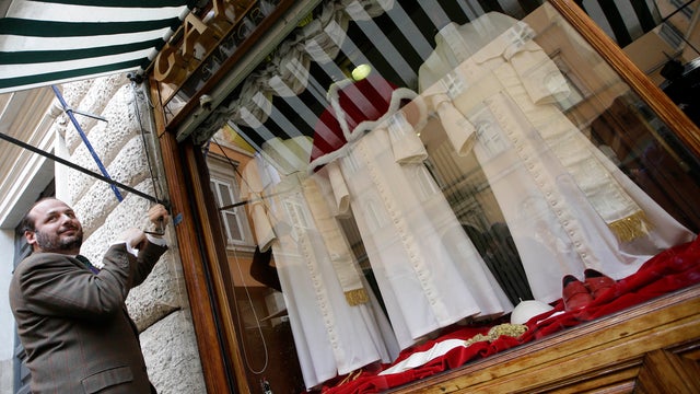 Lorenzo Gammarelli pulls sun shades over his shop window where three sets of papal outfits -- small, medium and large sizes -- are on display 