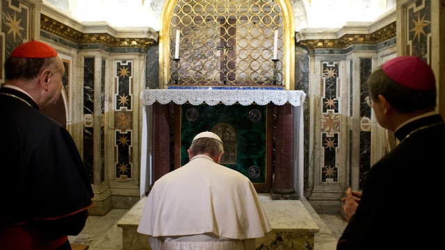 Pope Francis, flanked by Cardinal Angelo Comastri, left, and Bishop Vittorio Lanzani, right, kneels in prayer in front of what is believed to be the burial site of St. Peter's in the necropolis where pagans and early Christians were buried under St. Peter 