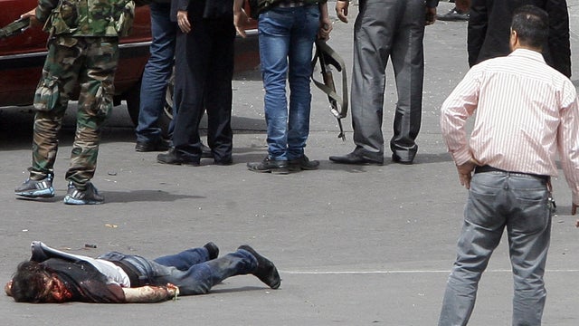 Severely wounded man lies on ground as security forces inspect scene of deadly car bomb explosion that rocked central Damascus on April 8, 2013. State-run TV says it killed at least 12 people and blamed what it called terrorist suicide bombing.  