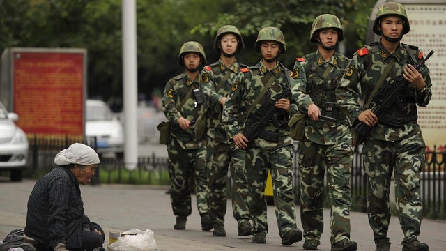 A Muslim Uighur woman begs as armed Chinese paramilitary police march past on a street in Urumqi, the capital of the Xinjiang region 