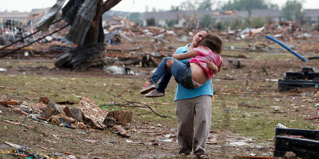 A woman carries her child through a field near the collapsed Plaza Towers Elementary School in Moore, Okla., Monday, May 20, 2013. 