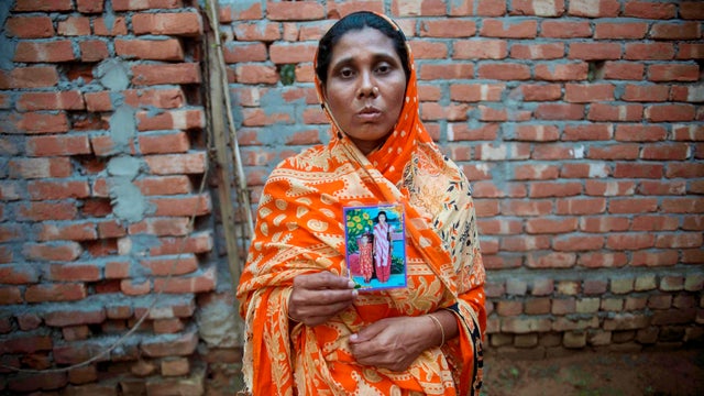 Hawa Begum holds a photograph of her two daughters outside the family home in Tekani  