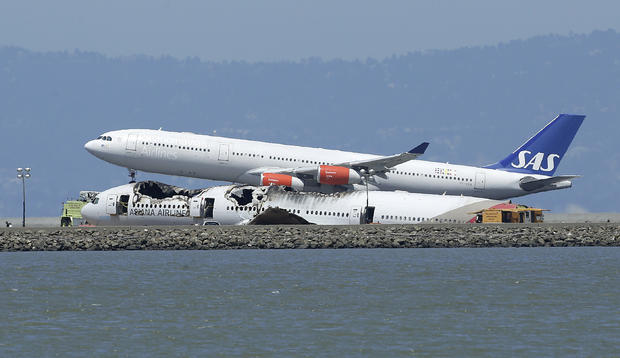 The wreckage of Asiana Flight 214 that crashed upon landing Saturday sits on the tarmac at San Francisco International Airport as a Scandinavian Airlines plane lands Monday, July 8, 2013 in San Francisco. Investigators said the Boeing 777 was traveling "s 