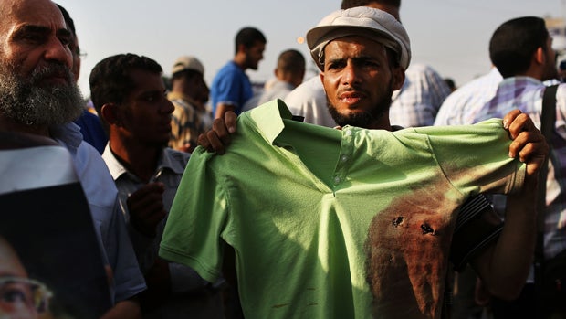 A man holds up a bloodied shirt with bullet holes at a pro Mohamed Morsi rally near where over 50 were purported to have been killed by members of the Egyptian military and police in early morning clashes on July 8, 2013 in Cairo, Egypt.  