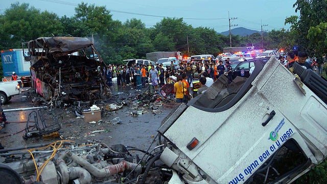 Charred wreckage of a double-decker passenger bus, top left, sits in the middle of a highway after a collision with a truck 