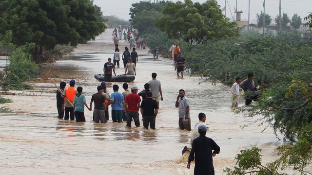 People wade through flooded road caused by heavy rains on the outskirts of Karachi, Pakistan 