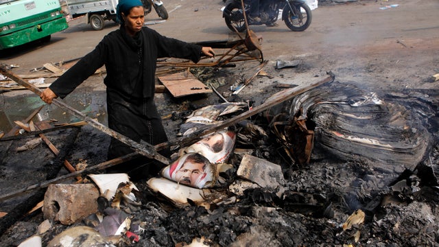 An Egyptian woman searches for useful items near burned posters of Egypt's ousted President Mohammed Morsi in Nahda Square, near Cairo University in Giza 