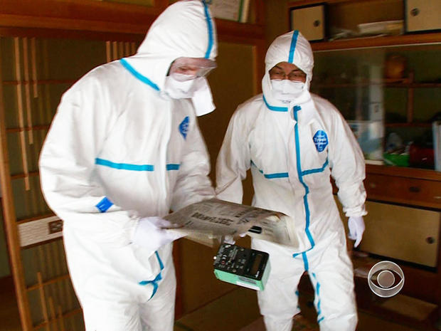 Akira Okawara and Seth Doane wear protective suits to travel to Okuma. 