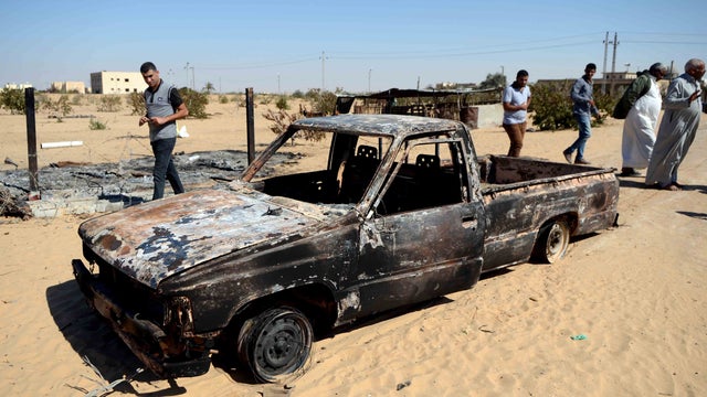Egyptians walk past the wreckage of a burnt car the day after an attack by the Egyptian Army in a village on the outskirts of the Northern Sinai town of Sheik Zuweid 